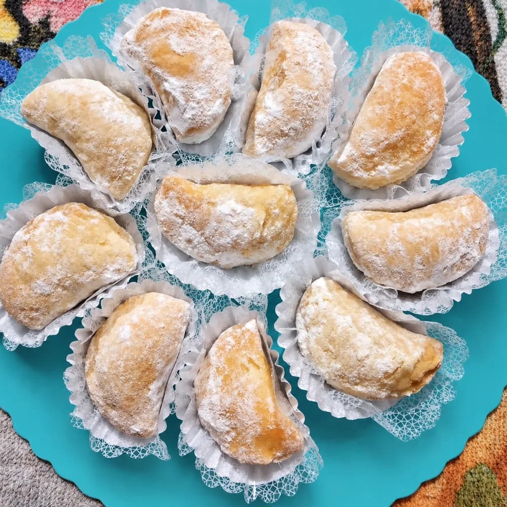 Bocaditos de hojaldre rellenos y espolvoreados con azúcar impalpable, dispuestos en círculo sobre un plato celeste