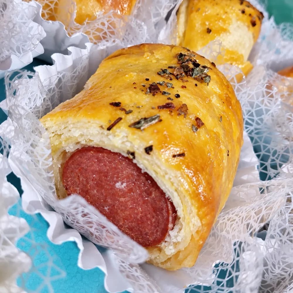 Primer plano de un saladito de masa casera dorada relleno con salame, servido en un pirotín de papel